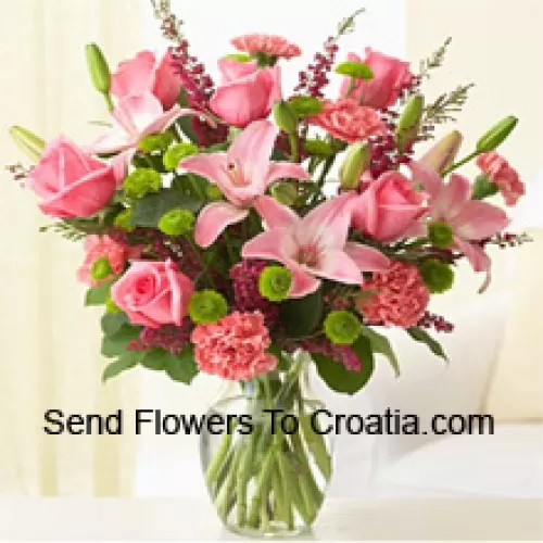 Trandafiri roz, garoafe roz și crini roz împreună cu ferigi și umpluturi asortate într-un vas de sticlă