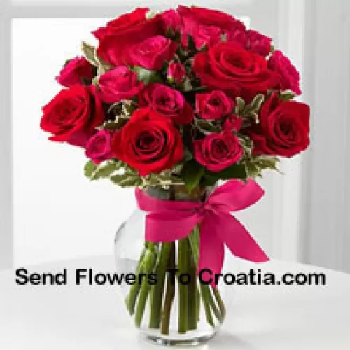 19 красных роз с сезонными наполнителями в стеклянной вазе, украшенной розовым бантом
